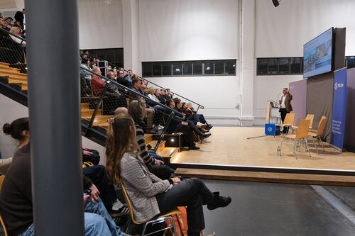 A room with a person at the lectern and people sitting on a staircase