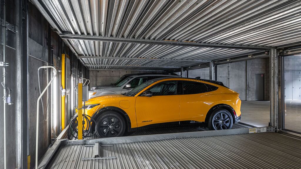 The image shows a car on a platform inside an automated parking system in a modern underground garage.
