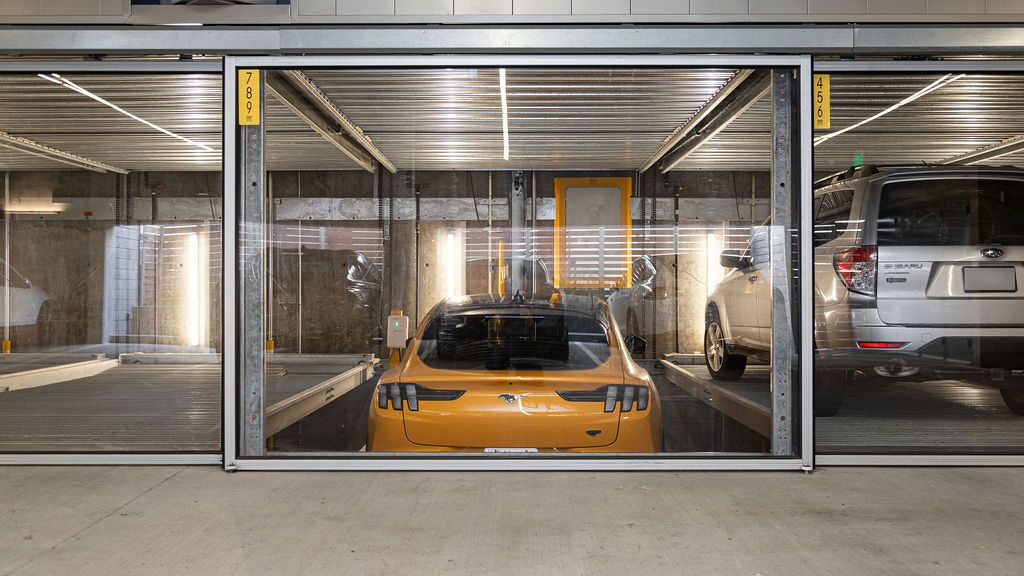 The image shows a yellow sports car in a parking system inside a modern underground garage.