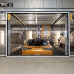 The image shows a yellow sports car in a parking system inside a modern underground garage.