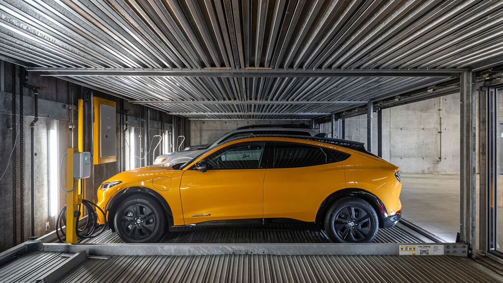The image shows a car on a platform inside an automated parking system in a modern underground garage.