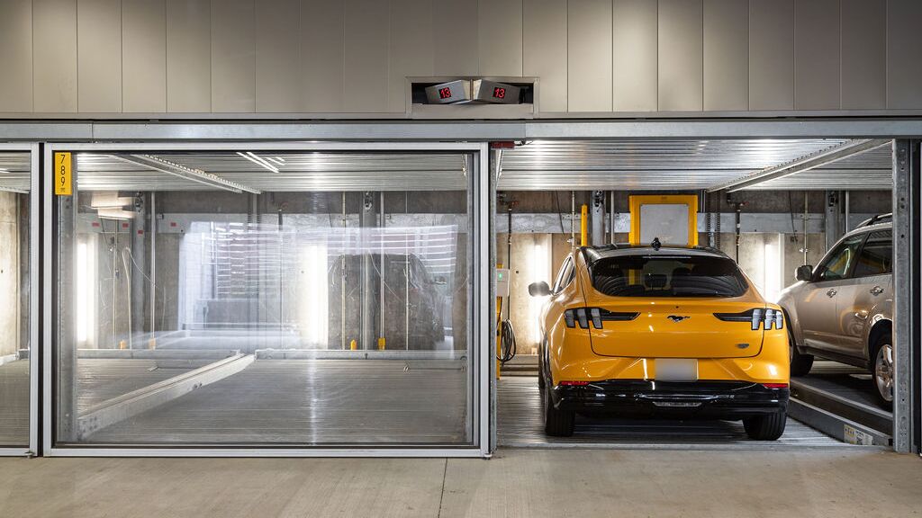 The image shows several vehicles in glazed parking spaces of a parking system in a modern underground garage.
