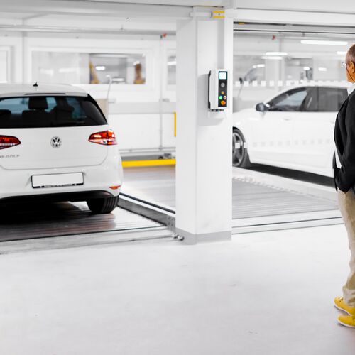 A man stands in front of a parking system with cars
